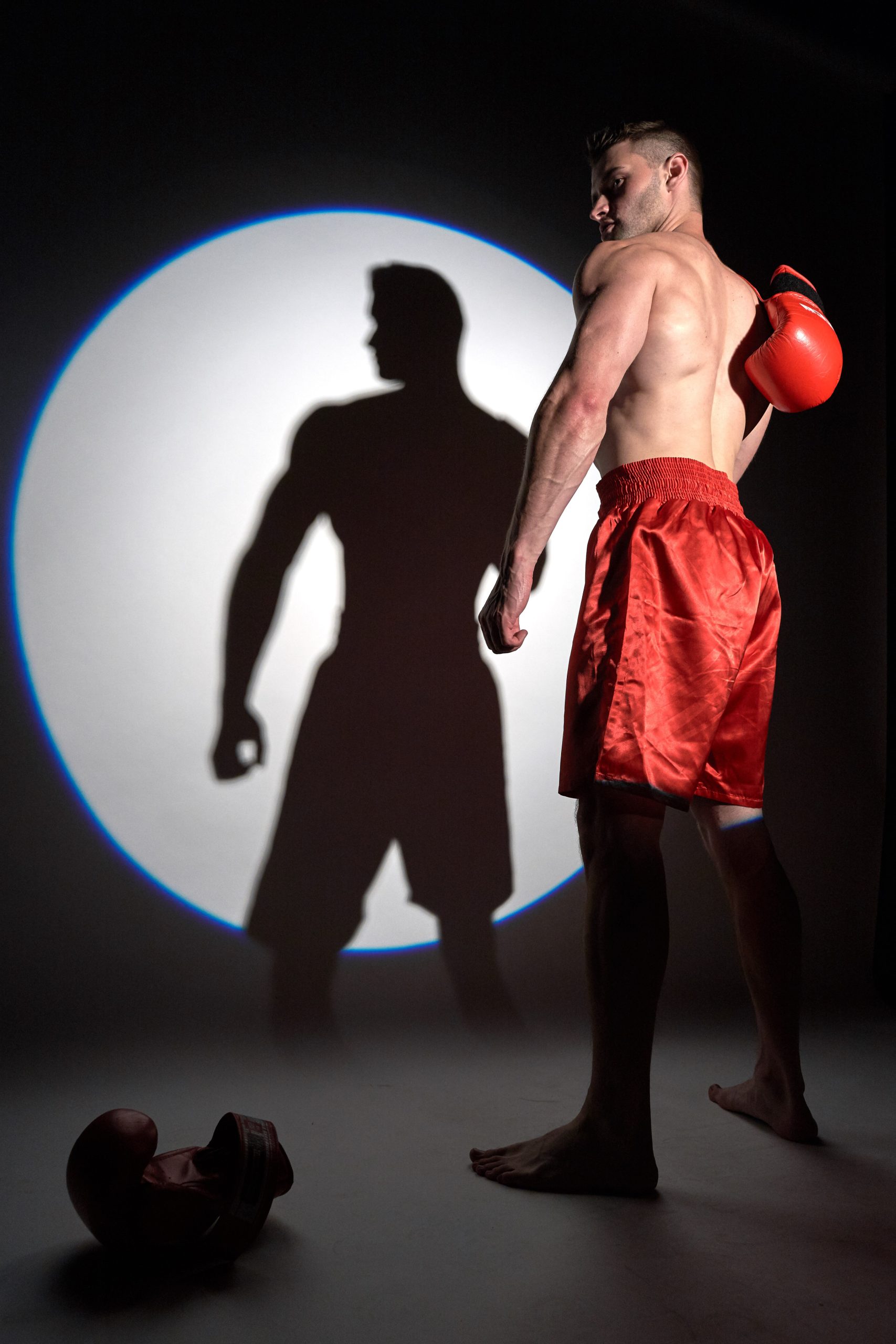 Accueil 2 Comment s'en sortir? Boxeur torse nu en short rouge avec gants de boxe, regardant son ombre projetée sur un mur éclairé. Comment s'en sortir ?